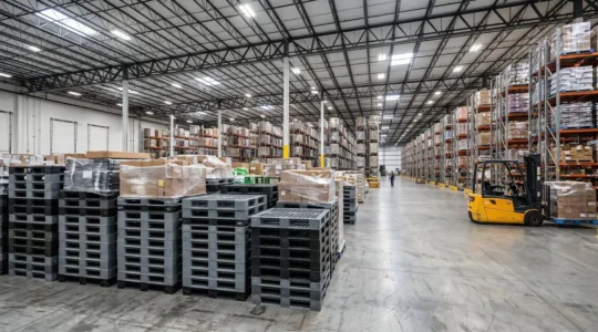 Palettes en plastique recyclé empilées dans un entrepôt logistique moderne avec chariots élévateurs